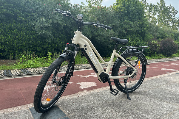 Sand beige HJM Radiant step-through electric bike parked beside a red cycling path, viewed from the front left.